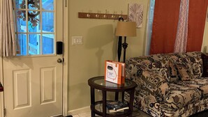 A living room with a patterned sofa, a glass coffee table with a book, a lamp, and a coat rack. - Delightful Atlanta family- sized apt. Sleeps 6 & pet friendly. (Atlanta)
