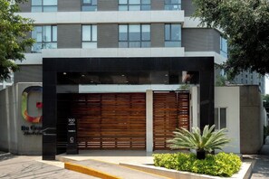 Une entrée moderne avec une façade noire, un portail en bois à lattes et un petit espace jardin agrémenté de plantes.