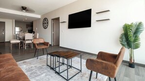 Un salon moderne comprenant un canapé, deux fauteuils, une table basse et un téléviseur fixé au mur.