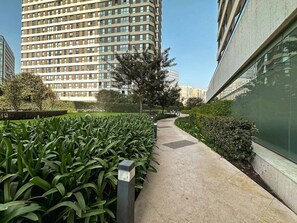 Un chemin bordé de verdure et une façade de bâtiment moderne.