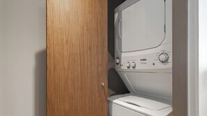 Une machine à laver blanche, dotée de boutons de commande et d’une porte en bois entrouverte.