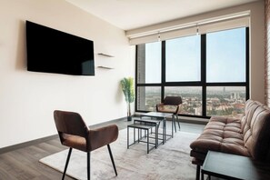 Un salon moderne doté d’un téléviseur à écran plat, de meubles en cuir et d’une grande fenêtre offrant une vue sur la ville.
