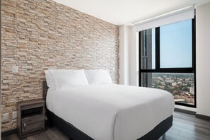 Une chambre moderne avec un mur en pierre, un grand lit, une table de chevet et une vue sur la ville par une grande fenêtre.