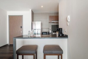 A modern kitchen with a central island, two bar stools, a refrigerator, microwave, and a coffee maker.