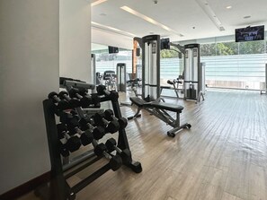 Een sportschool met fitnessapparatuur, waaronder gewichten en een bank.
