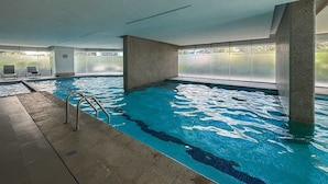 Une piscine intérieure à l’eau claire, avec un escalier et une vue sur l’extérieur.