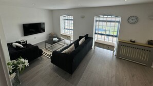 A modern living room with a black sofa, a coffee table, a TV, and two windows with blinds. - Luxury Loft Style 2 Bed Apartment Next to Excel/o2 (London)