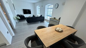 A modern living room with a black sofa, a wooden dining table with chairs, and a TV mounted on the wall. - Luxury Loft Style 2 Bed Apartment Next to Excel/o2 (London)