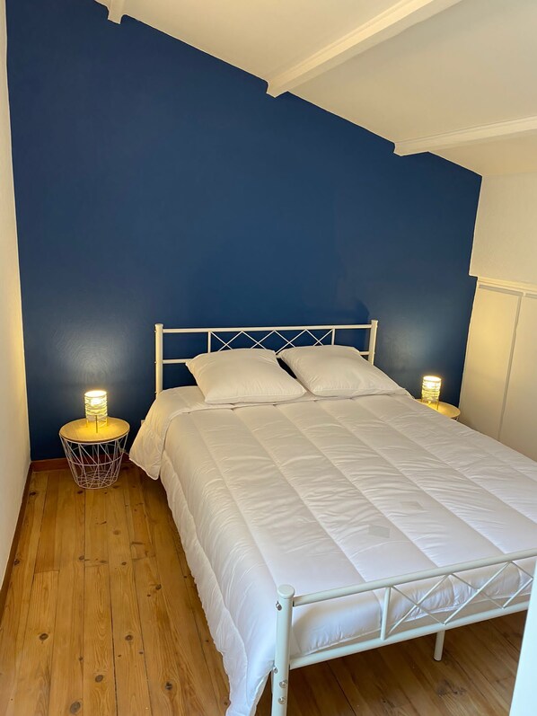 A single bed with a white metal frame and white bedding in a room with dark blue walls and wooden flooring.