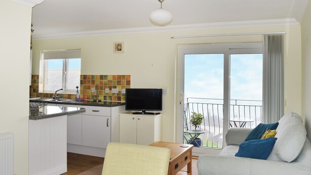 A compact living space with a kitchenette, a television, a balcony with a view, and a sofa with cushions. - 1 bedroom accommodation in Ventnor (Ventnor)