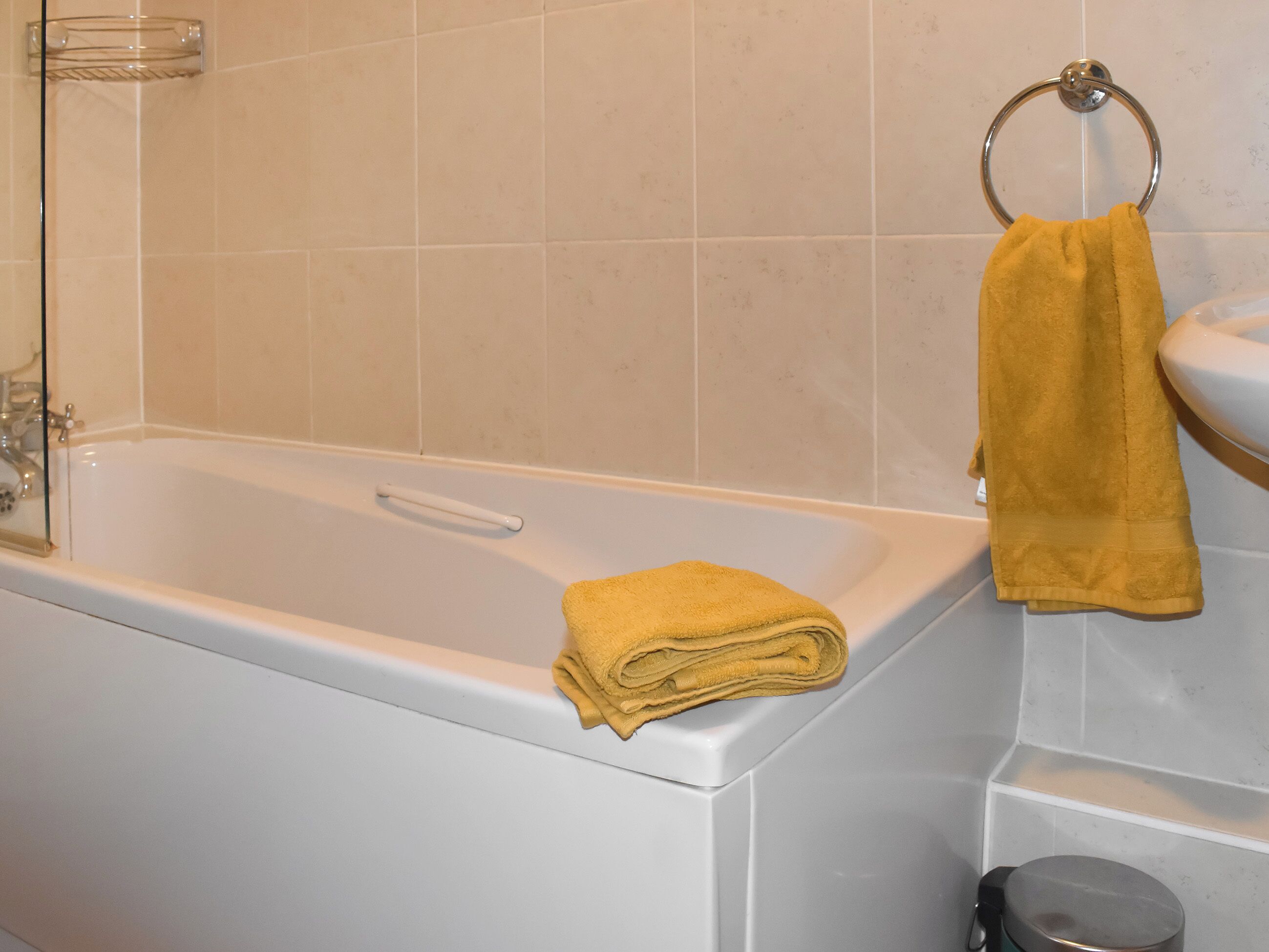 A bathroom with a bathtub, a glass shower enclosure, and a towel rack with a yellow towel.