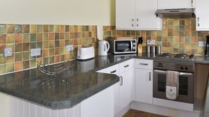 A kitchen with white cabinets, a microwave, a toaster, and a stove. - 1 bedroom accommodation in Ventnor (Ventnor)