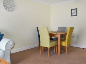 A dining area with a round wooden table and four chairs, a clock on the wall, and a framed picture. - 1 bedroom accommodation in Ventnor (Ventnor)