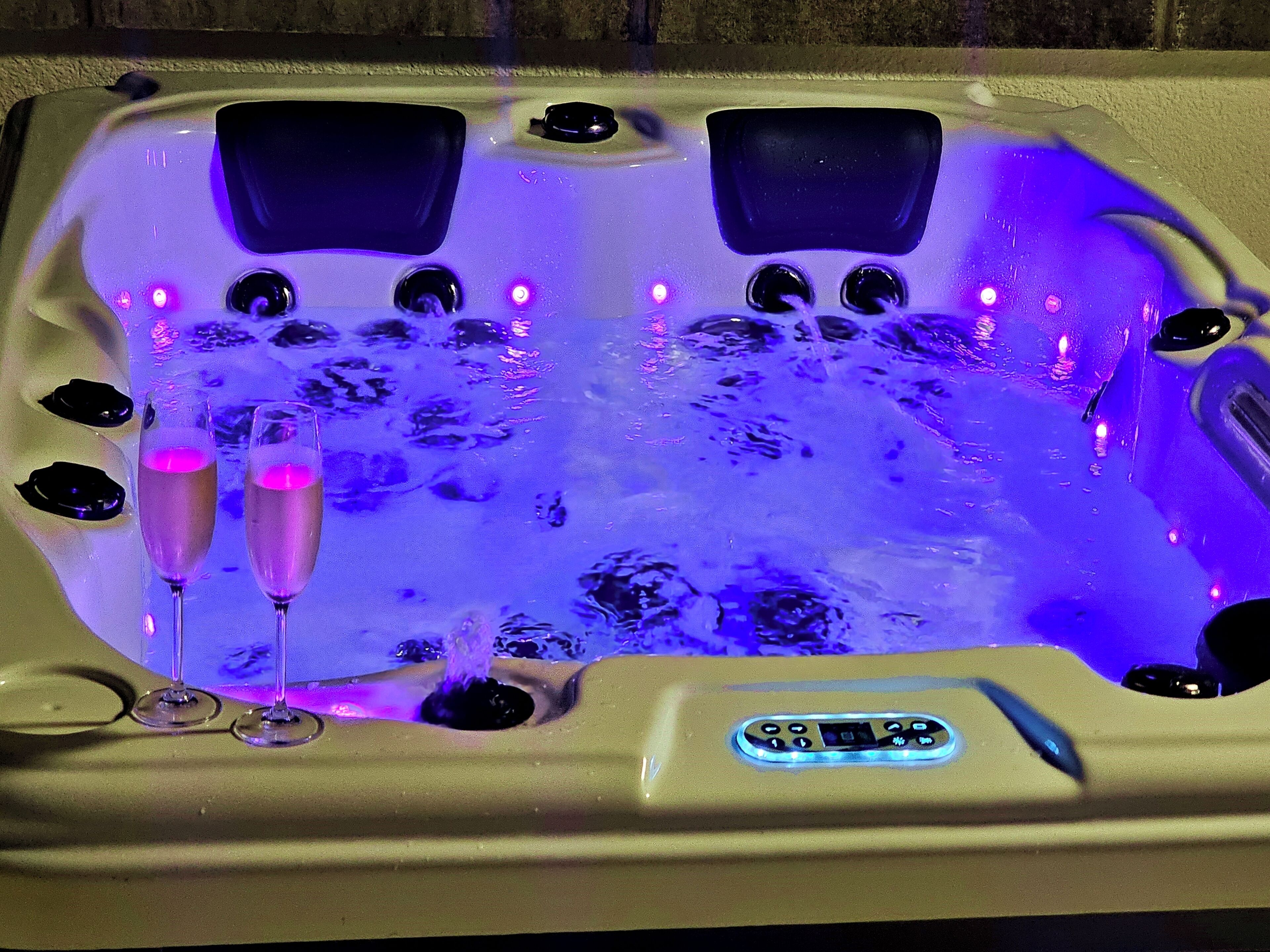A hot tub with multiple jets, a control panel, and two champagne flutes.