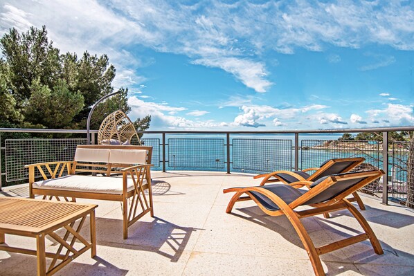 Une terrasse avec des meubles en bois, une piscine et une vue sur la mer.