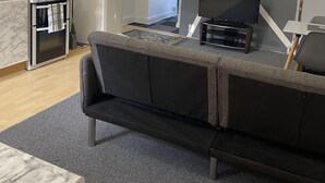 Un salon moderne avec un canapé gris, un téléviseur à écran plat et un coin cuisine comprenant un réfrigérateur blanc et une cuisinière.