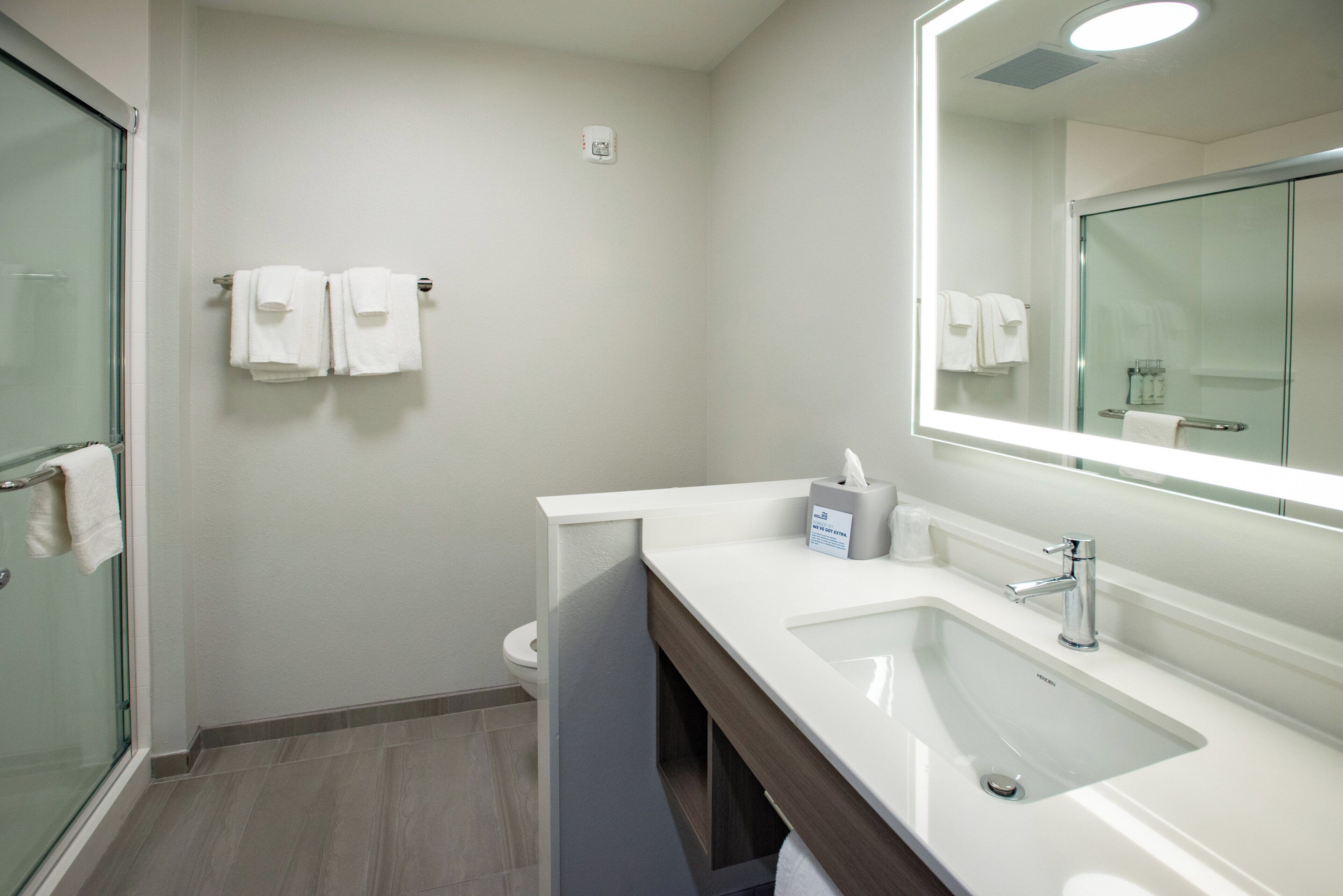 Un baño moderno con cabina de ducha de vidrio, lavamanos blanco con espejo y toallero.