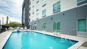 A rectangular swimming pool with a tiled edge, adjacent to a modern building with large windows and a grey facade. - Holiday Inn Express & Suites Pensacola Airport North – I-10 by IHG (Pensacola)