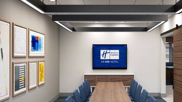 Un salón de conferencias con una larga mesa, sillas azules, obras de arte enmarcadas en las paredes y un letrero de Holiday Inn Express.