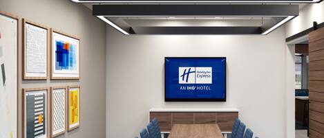 Un salón de conferencias con una larga mesa, sillas azules, obras de arte enmarcadas en las paredes y un letrero de Holiday Inn Express.