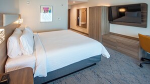 A hotel room with a large bed, a TV mounted on the wall, a wooden wardrobe, and a desk with a chair. - Holiday Inn Express & Suites Pensacola Airport North – I-10 by IHG (Pensacola)