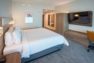 Une chambre d’hôtel avec un grand lit, un téléviseur fixé au mur, une armoire en bois et un bureau avec une chaise.