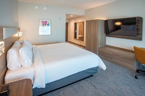 Une chambre d’hôtel avec un grand lit, un téléviseur fixé au mur, une armoire en bois et un bureau avec une chaise.