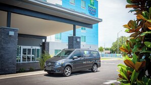 A Holiday Inn Express & Suites building with a modern design, featuring a blue facade and a parking area with a Mercedes-Benz van. - Holiday Inn Express & Suites Pensacola Airport North – I-10 by IHG (Pensacola)