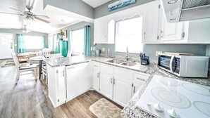 A modern kitchen with white cabinets, a granite countertop, a built-in microwave, and a stove. - 708 Seagull Dr. - King, Queen & Queen - Includes Golf Cart & Wifi! (Panama City Beach)