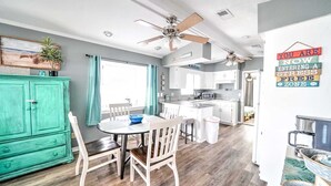 A compact kitchen with white cabinets, a dining area with a round table and chairs, and a teal cabinet. - 708 Seagull Dr. - King, Queen & Queen - Includes Golf Cart & Wifi! (Panama City Beach)