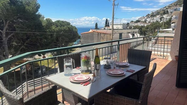 A balcony with a table set for dining, overlooking a coastal town.
