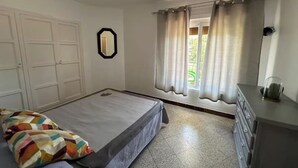 A bedroom with a bed, a dresser, a window with curtains, and a door.