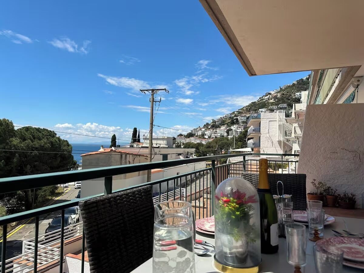Ein Balkon mit Esstisch, der auf eine Küstenstadt mit Häusern und blauem Himmel blickt.