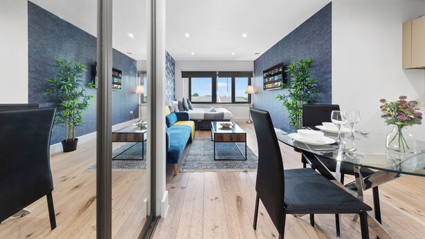 A modern dining area with a glass table, black chairs, and a blue sofa in the background. - Charming 1-bed Apartment in London (Hayes)