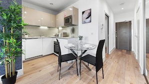 A modern kitchen with white cabinets, a microwave, and a dining area with a glass table and black chairs. - Charming 1-bed Apartment in London (Hayes)