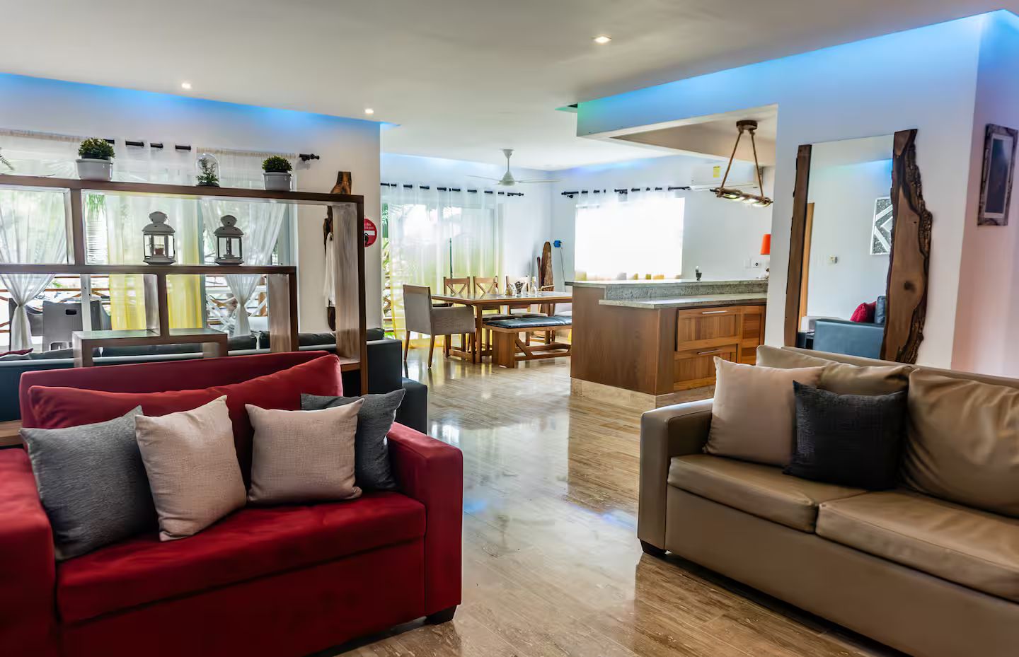Een ruime woonkamer met een rode bank, een beige bank en een eethoek met een tafel en stoelen.