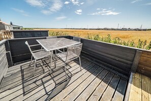 En udendørs terrasse med et metalbord og stole, med udsigt over et marklandskab.