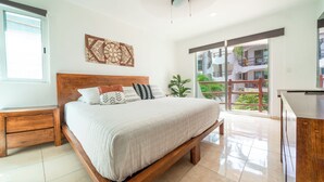 A bedroom with a large bed, wooden headboard, and a view of a balcony with plants.