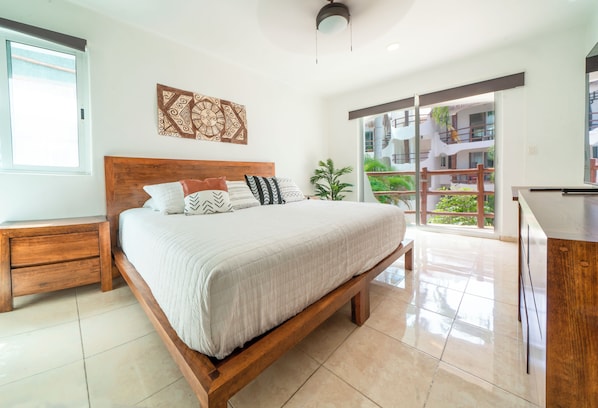 A bedroom with a large bed, wooden headboard, and a view of a balcony with plants.