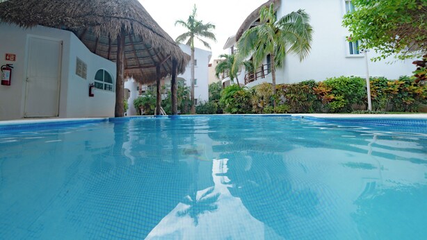 A swimming pool with a tiled floor, surrounded by white buildings with thatched roofs and palm trees.