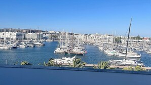 Un puerto deportivo con numerosos veleros amarrados, rodeado de edificios y palmeras.