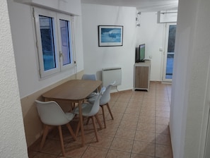 A dining area with a wooden table and four chairs, a framed picture on the wall, and a television on a cabinet. - 1 Bedroom Apartment in Anglet (Anglet)