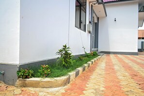 Stroll through the beautifully landscaped garden, featuring a paved walkway and a small garden area with lush greenery and vibrant flowers.