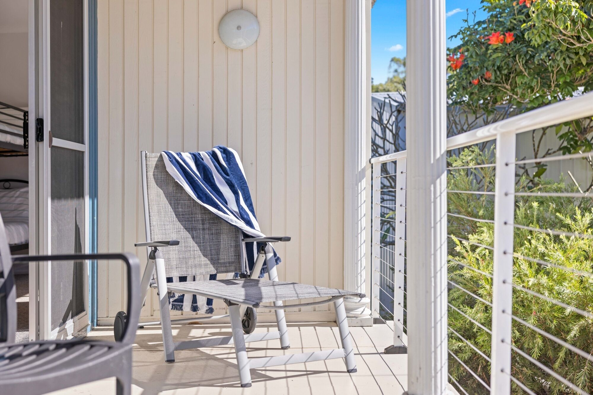 A balcony with a chair covered by a striped towel, a small table, and a railing.