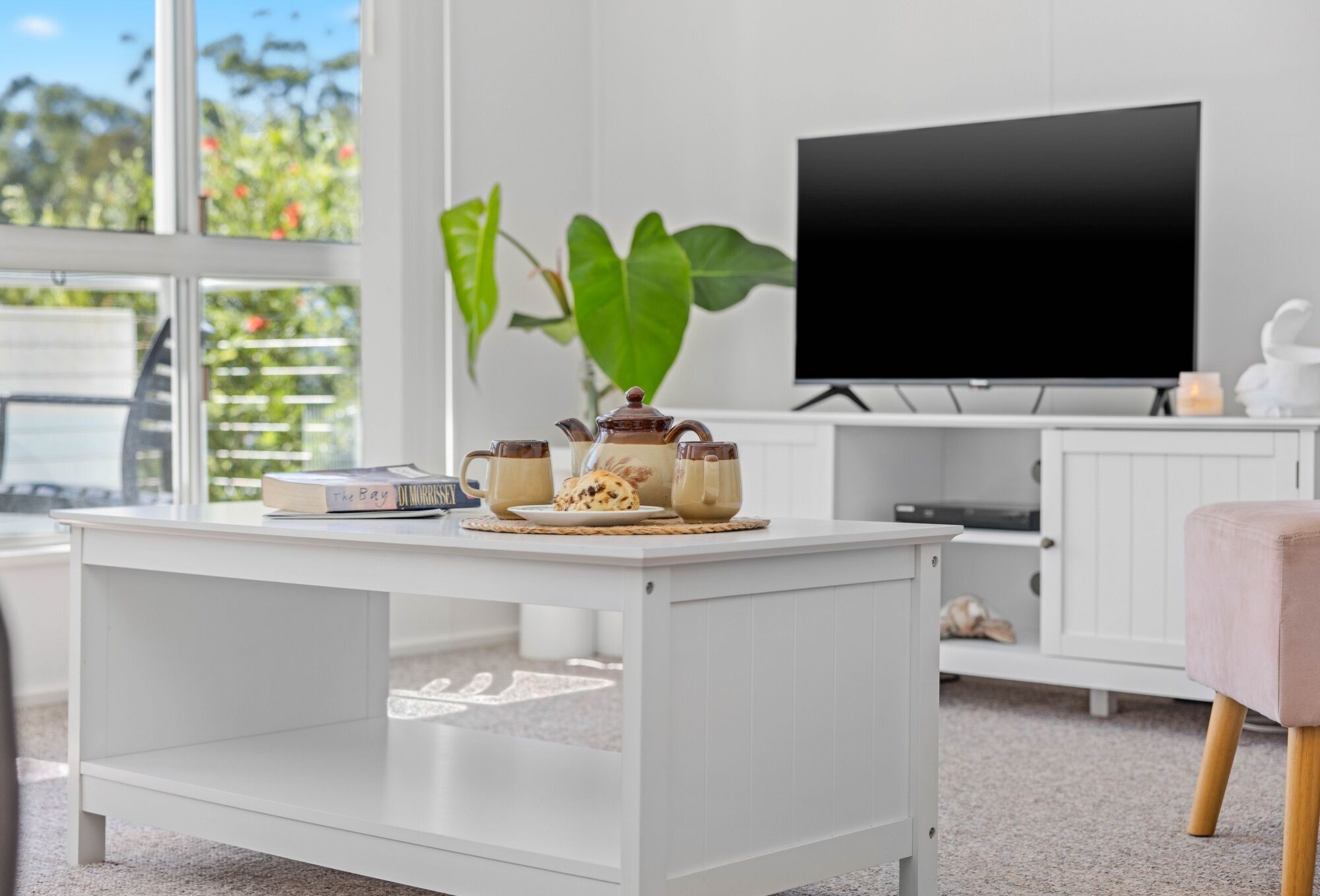 Een moderne woonkamer met een witte salontafel, een televisie en een plant.