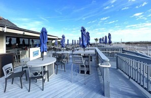 A deck with tables and chairs, blue umbrellas, and a railing overlooking a beach. - Beach & Tennis Resort Villa (Hilton Head Island)