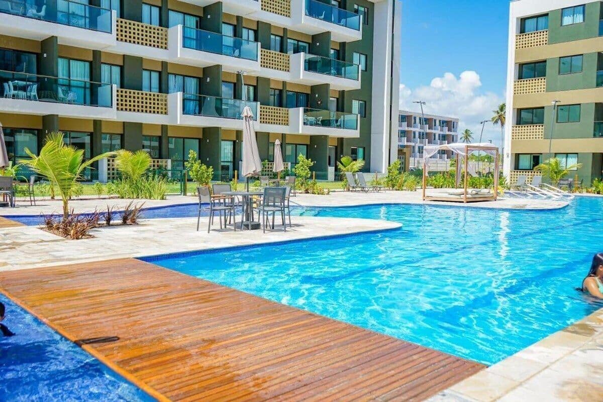 A modern hotel with a swimming pool, outdoor seating, and a multi-story building with balconies.