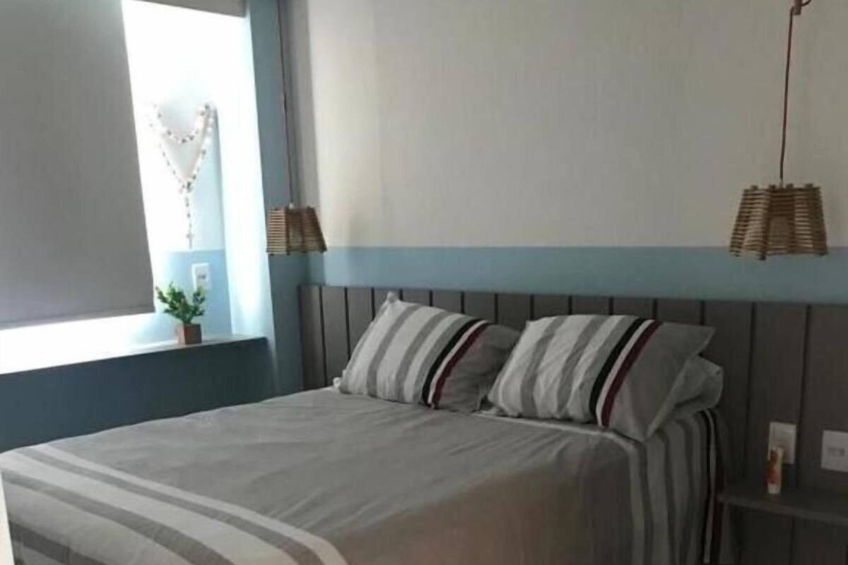 A bedroom with a bed, a window, a bedside table, and a hanging light fixture.
