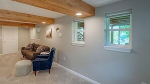 A spacious room with a high ceiling, a brown couch, a blue chair, and two windows with blinds.