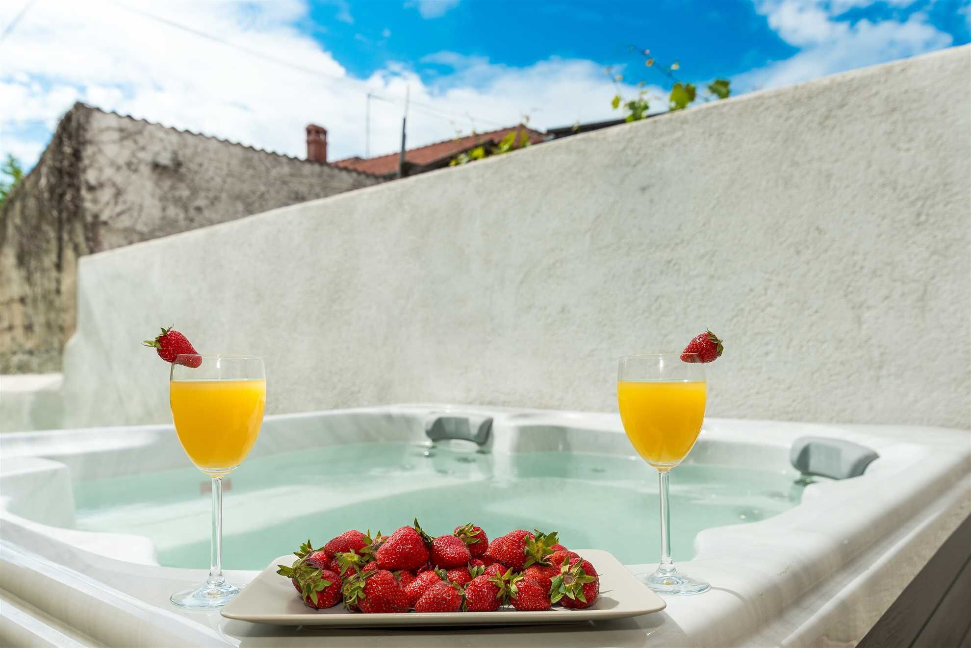 A hot tub with two glasses of orange juice and a plate of strawberries.